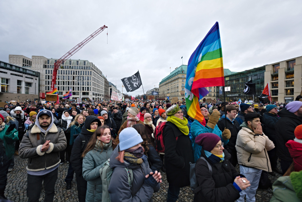 Große Gruppe von Menschen mit LGBTQ+-Rechten-Schildern vor einem Gebäude in Berlin, mit einem Kran und einem bewölkten Himmel im Hintergrund.