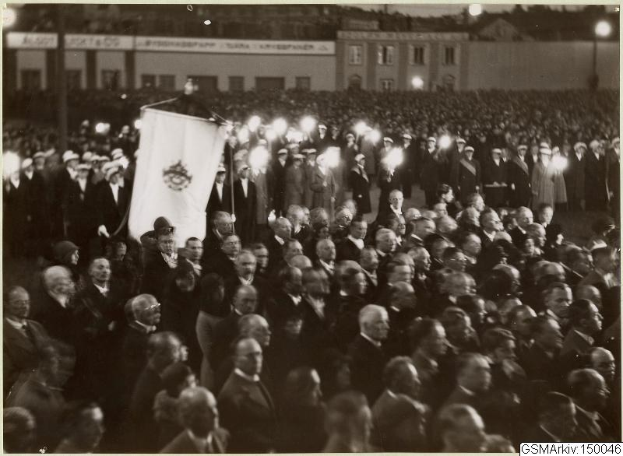 Schwarzes und weißes Bild einer großen Menge vor einem Gebäude, mit einer Person, die eine Fahne hält, in der Mitte, Polen und Lichter im Hintergrund und Text unten, der 'Gustav Klimts Rede an der Berliner Mauer' lautet.