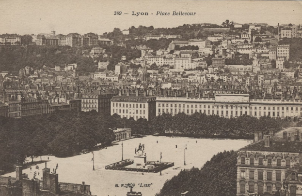 Ein altes Schwarz-Weiß-Foto einer Stadt mit vielen Gebäuden, Bäumen, Pfählen und einem zentralen Brunnen mit Text oben.