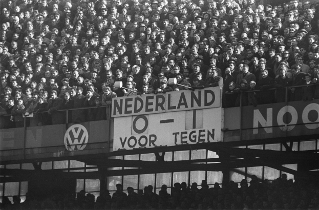 Ein Schwarz-Weiß-Foto einer großen Menschenmenge in einem Stadion, mit einer Texttafel in der Mitte und ein paar Individuen unten.