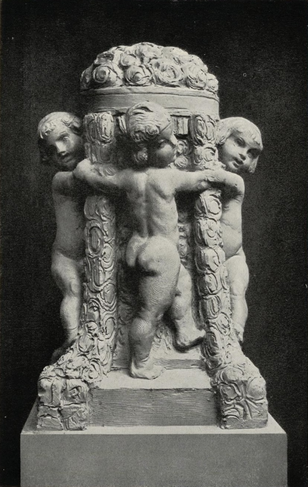 Ein Schwarz-Weiß-Foto einer Skulptur mit drei Cherubinen in langen Gewändern, die nebeneinander auf einem verzierten steinernen Sockel stehen, mit ausgestreckten Armen und geneigten Köpfen.