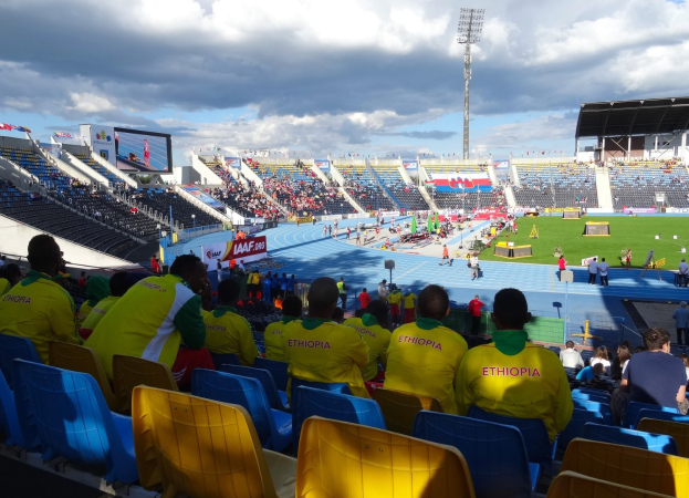 Ein voller Stadion mit Zuschauern bei einem Fußballspiel, mit Bannern, Anzeigetafel, Metalldach und bewölktem Himmel.