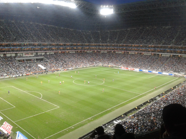Ein hell erleuchtetes Fußballstadion voller jubelnder Fans, die ein Spiel verfolgen, umgeben von Werbetafeln.