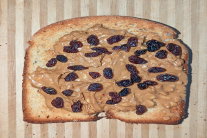 Ein Brotstück mit Erdnussbutter und Rosinen auf einer hölzernen Oberfläche.