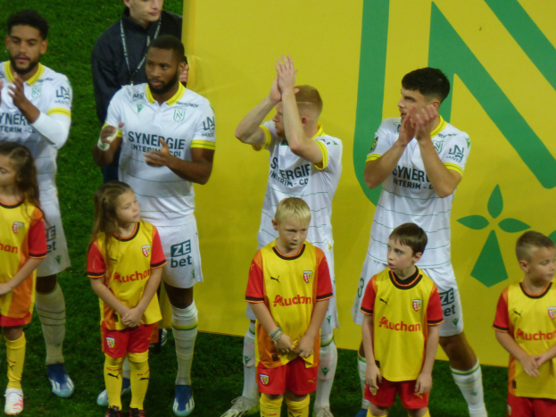 Eine Gruppe junger Fußballspieler in Uniformen klatscht auf einem Ligue-1-Feld, mit einem "Ligue-1"-Schild im Hintergrund.