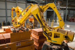 Ein großes Lager mit zahlreichen Kisten, Kränen, einem Zaun, Pfählen und anderen Gegenständen, mit einer Wand im Hintergrund, die eine industrielle Umgebung andeutet.