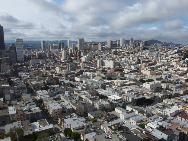 Eine dicht bebaute Stadtlandschaft mit zahlreichen Häusern, Gebäuden und hohen Türmen, mit minimaler Vegetation und einem klaren Himmel im Hintergrund.
