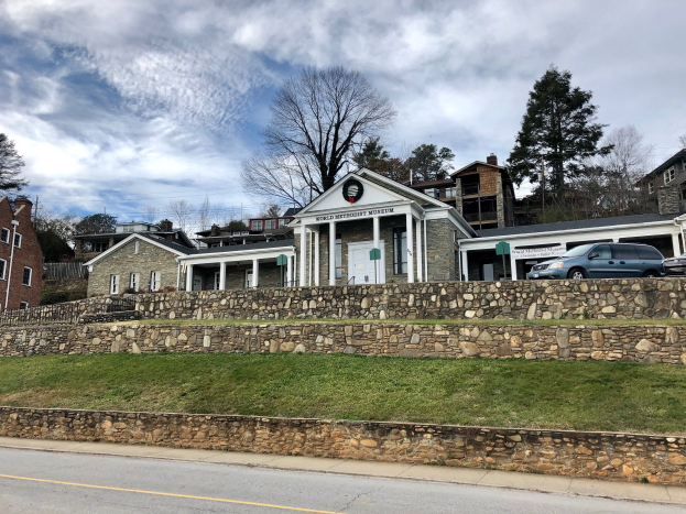 Steinwand mit parkenden Autos, angrenzende Gebäude mit Fenstern und Türen, Bäume und ein bewölkter Himmel im Hintergrund, als Weltkulturerbe-Museum bezeichnet.