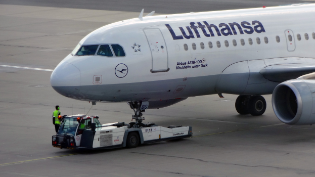 Ein Lufthansa Airbus A319-100 steht auf dem Rollfeld am Frankfurter Flughafen, mit einem Fahrzeug und einer Person in der Nähe, bereit zum Start.