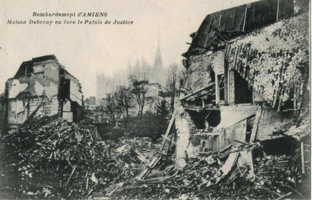 Ein Schwarz-Weiß-Foto eines zerstörten Gebäudes in einer Stadt, umgeben von Bäumen und anderen Gebäuden, mit dem Text "Bombardement d'Amiens Maison Deberry en Face de la Palais de Justice" oben.