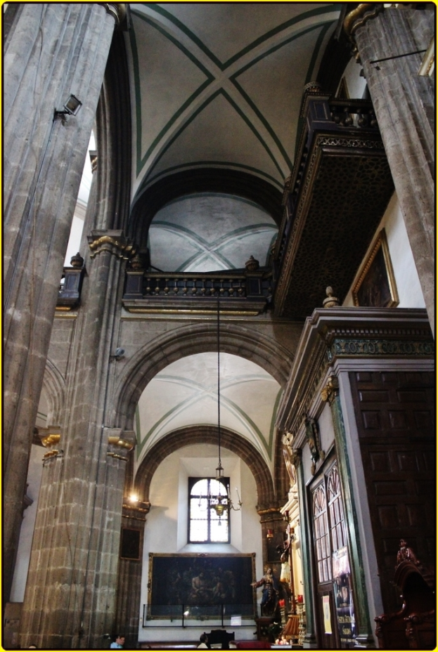 Ein Innenblick in einen Palast mit Schränken, beleuchteten Säulen, Wandskulpturen, einem großen Rahmenbild und einer Deckenleuchte.