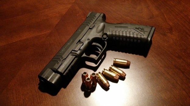 Schwarze Sig Sauer P320 X-Five Pistole mit langem Lauf und 9mm Magazinkapazität, zusammen mit mehreren Patronen in verschiedenen Größen und Farben auf einem Holztisch präsentiert.