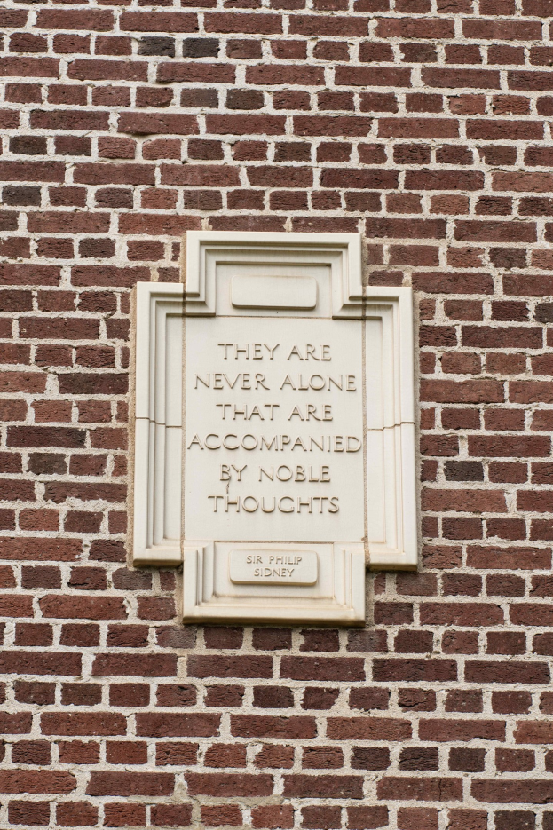 Steintafel an einer Backsteinwand mit fettgedrucktem Text "Sie sind nie allein, die von edlen Gedanken begleitet sind."