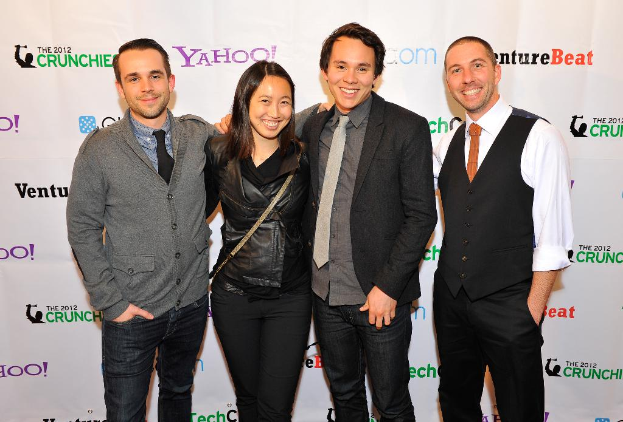 Eine Gruppe von l├Ąchelnden Menschen, die für ein Foto mit einem Sponsorenbanner im Hintergrund posen.