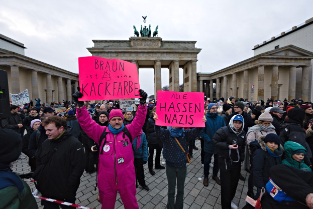 Eine Gruppe von Menschen mit Protestschildern vor dem Reichstagsgebäude in Berlin, mit Gebäuden und Statuen im Hintergrund.