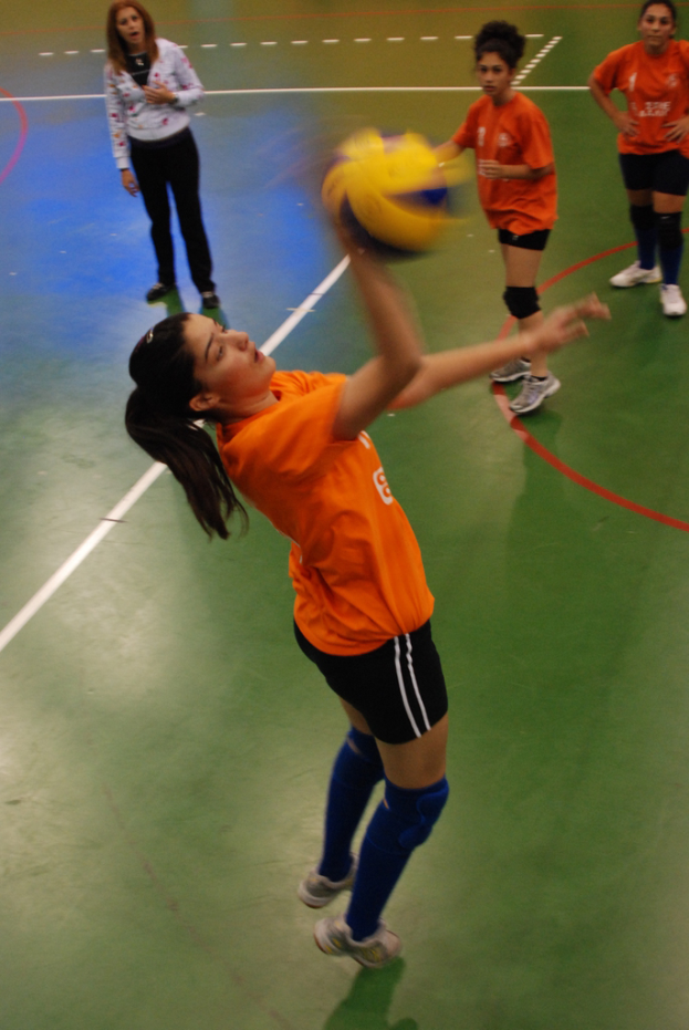 Eine Volleyballerin schlägt den Ball, während zwei andere Spieler und eine weitere Frau zuschauen.