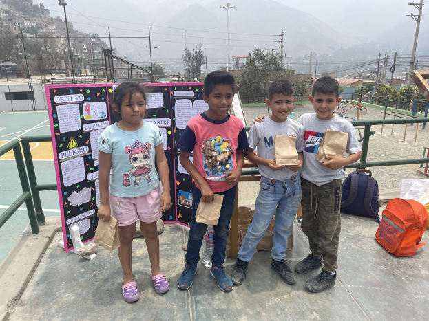 Gruppe von Kindern, die Papiertüten auf einem Basketballfeld mit Ausrüstung und einer Tafel im Hintergrund halten.
