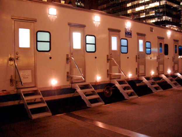 Ein Zug mit Lichtern in der Mitte, umgeben von Gebäuden im Hintergrund und einem Boden unten.