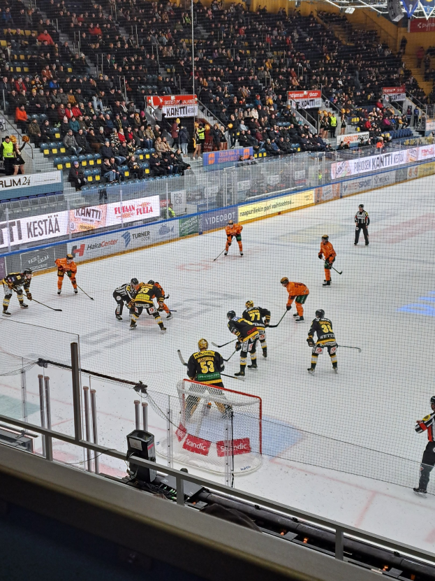 Gruppe von Menschen, die Hockey auf einem Eisstadion in einer Arena mit Zuschauern im Hintergrund und beleuchteter Beleuchtung oben spielen.