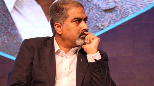 Ein Mann im Anzug sitzt auf einer Bühne und schaut nachdenklich auf einen Bildschirm.