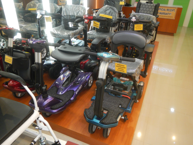 Eine Reihe von E-Scootern in einem Geschäft aufgereiht, jeder mit einem Preisschild, und ein Holztisch mit einer Tafel im Hintergrund.