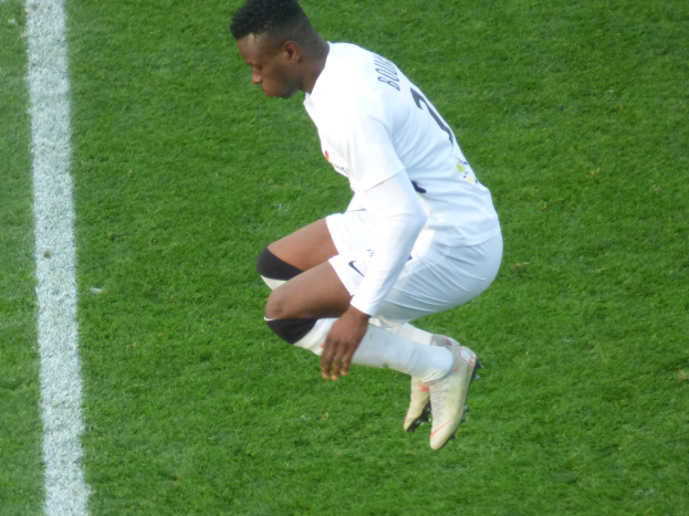 Ein Mann in weißer Uniform kniet auf einem Fuballfeld, tr"gt Fuballschuhe und hat eine weiße Linie auf der linken Bildseite.