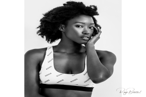 Ein Schwarz-Weiß-Foto einer Frau in einem Sport-BH, mit einem selbstbewussten und entschlossenen Gesichtsausdruck, ihre Haare zu einem glatten Pferdeschwanz gebunden und einem Wasserzeichen in der rechten unteren Ecke.