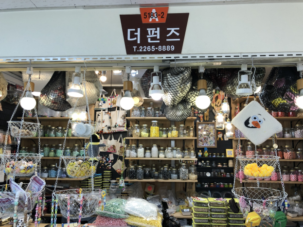 Ein unordentlicher Laden in Seoul mit verschiedenen Artikeln wie Körbchen, Lichtern, Flaschen und Spielzeugen auf Regalen, mit einer Tafel öberall, die ihn als einen der besten koreanischen Läden kennzeichnet.