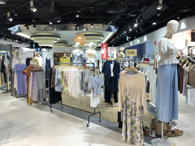 Ein hell erleuchteter Bekleidungsladen zeigt zahlreiche Kleider an Bügeln, Schaufensterpuppen, Informationsschildern und Bodenartikeln, was auf einen Modegeschäft hinweist.