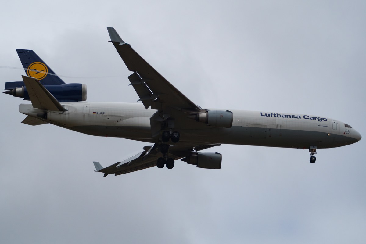 Lufthansa Cargo Boeing 777-300ER im Flug mit sichtbarem Text auf dem Rumpf, ausgefahrenen Flügeln, aktiven Triebwerken, gegen einen teilweise bewölkten Himmel.