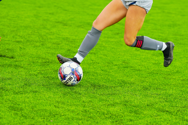 Eine Frau in einem Sportoutfit tritt einen Fußball auf einem saftig grünen Feld.