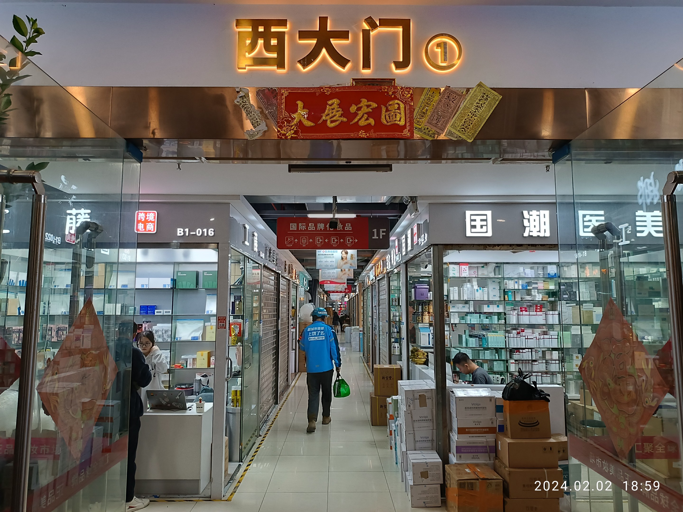 Innenansicht einer chinesischen Apotheke mit Glaswänden, Regalen voller Artikel, verstreuten Kartons, einer Pflanze links und einer Namensschild oben.