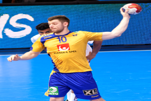 Ein Mann in einem gelben T-Shirt und blauen Shorts hält einen Handball auf einem Feld, mit einem Bildschirm im Hintergrund, der "Svenský Spel Handball World Cup 2019" anzeigt.