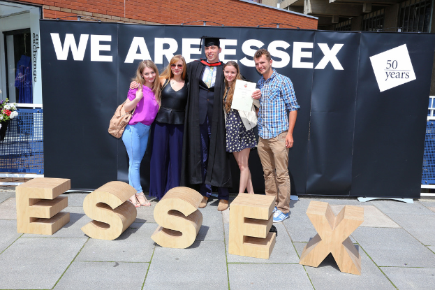 Eine Gruppe von Menschen, die mit einem Zertifikat in der Hand lächeln und vor einem Gebäude und einem Netz stehen.