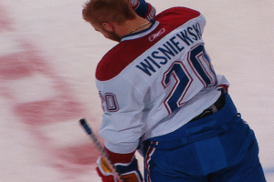 Ein Hockey-Spieler im 'Wisniewski'-Trikot steht auf dem Eis und hält einen Hockey-Schläger in der Hand, mit konzentriertem und entschlossenem Gesichtsausdruck.