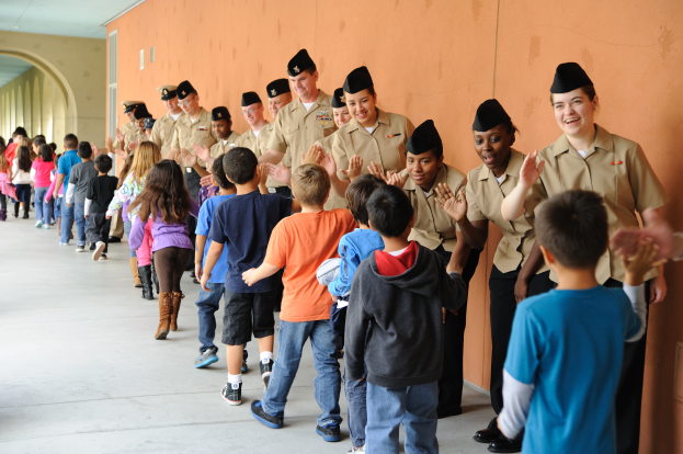 Eine Gruppe von Kindern in Uniformen, die einen Flur entlanggehen, mit einer Wand auf der rechten Seite und Lampen an der Decke.