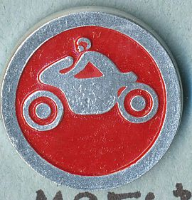 Ein rundes, rotes und silbernes Schild mit einer Person auf einem Motorrad, die einen Helm trägt, und wahrscheinlich der Name des Motorrads darauf geschrieben.