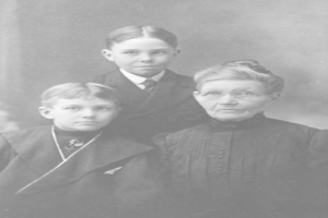 Ein Schwarz-Weiß-Vintage-Foto einer Frau mit Brille und zwei Jungen, die gemeinsam posieren, mit einem unscharfen Hintergrund.