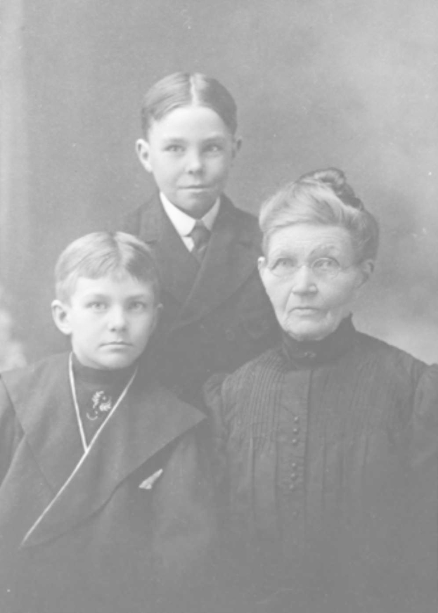 Ein Schwarz-Weiß-Vintage-Foto einer Frau mit Brille und zwei Jungen, die gemeinsam posieren, mit einem unscharfen Hintergrund.