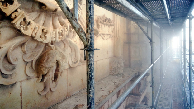 Gebäude mit detaillierten Schnitzereien an der linken Wand, Metallstangen an der rechten und Gerüst drumherum während der Renovierung.
