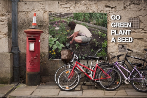 Fahrräder sind in der Nähe eines Briefkastens mit einer Sicherheitskegel auf der Spitze geparkt, mit einem Plakat an der Wand im Hintergrund und einem Weg am unteren Rand des Bildes.