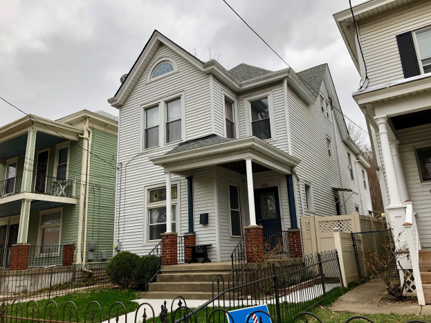 Eine Reihe von Häusern mit Fenstern, Türen, Säulen, Geländern, Stufen und Dächern, umgeben von einem Metallzaun, Gras, Pflanzen, Bäumen und einem bewölkten Himmel, mit einem Mietschild am unteren Rand, das die Adresse als 5901 S Elmwood Ave, Chicago 60618 angibt.