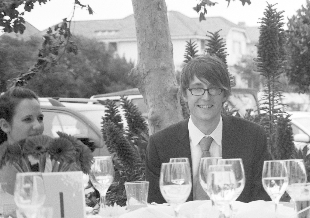 Ein Paar sitzt zusammen im Freien, mit Gläsern und Bäumen im Hintergrund, vor einem Haus.