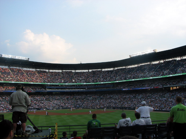 Eine Aufnahme eines Stadions mit Spielern auf einem Rasenfeld und Zuschauern in den Rängen, einige stehen in der Nähe der Vorderseite.