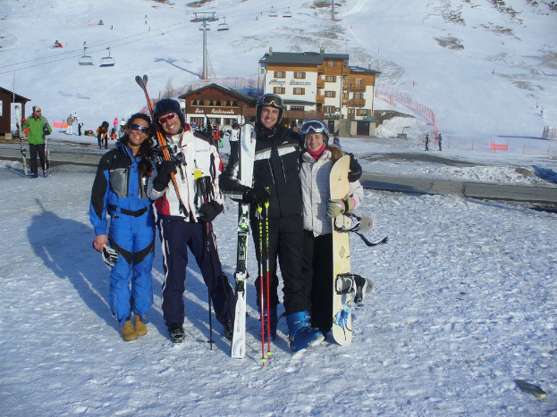 Vier Personen posieren für ein Foto mit Skate-Pads und Werkzeugen vor einem schneebedeckten Gebirge im Hintergrund.