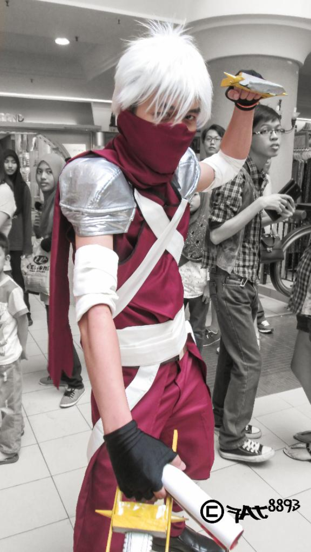 Eine Person mit einer Maske steht im Vordergrund mit mehreren Personen dahinter, und ein Lichtstrahl ist oben im Bild sichtbar.