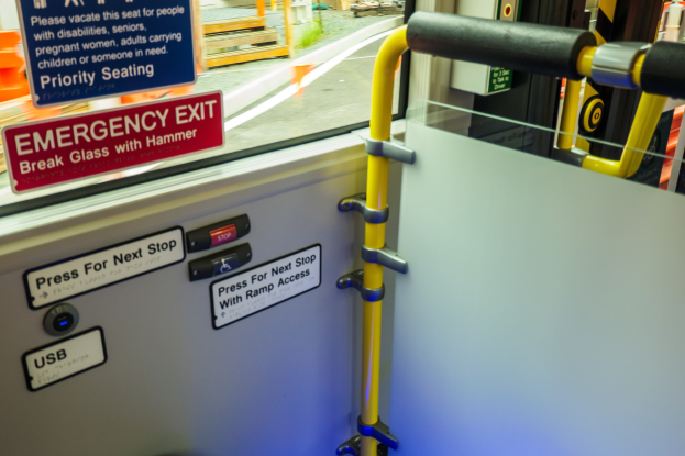 Notausgangsschild an einer Zugseite mit Tür, Griff und Glasfenster, das Straße, Pfähle und Außenobjekte zeigt.