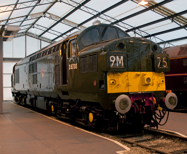 Ein Zug steht auf den Schienen neben einer Plattform mit einem Mast auf dem Dach, der Metallstangen und Lichter hat.